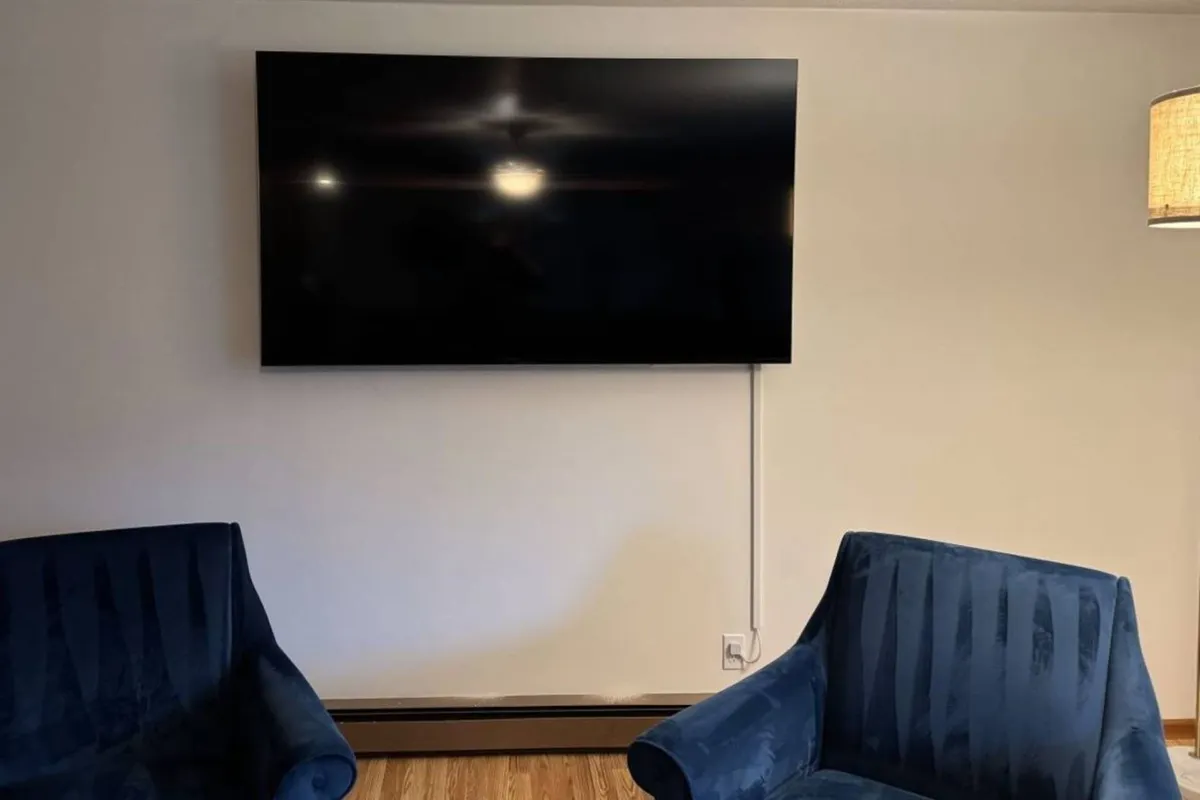 A spacious living area featuring a large television as a focal point, surrounded by blue armchairs and a lamp. The setup is ideal for movie marathons, game nights, and relaxed socializing, reflecting modern comfort and entertainment amenities.
