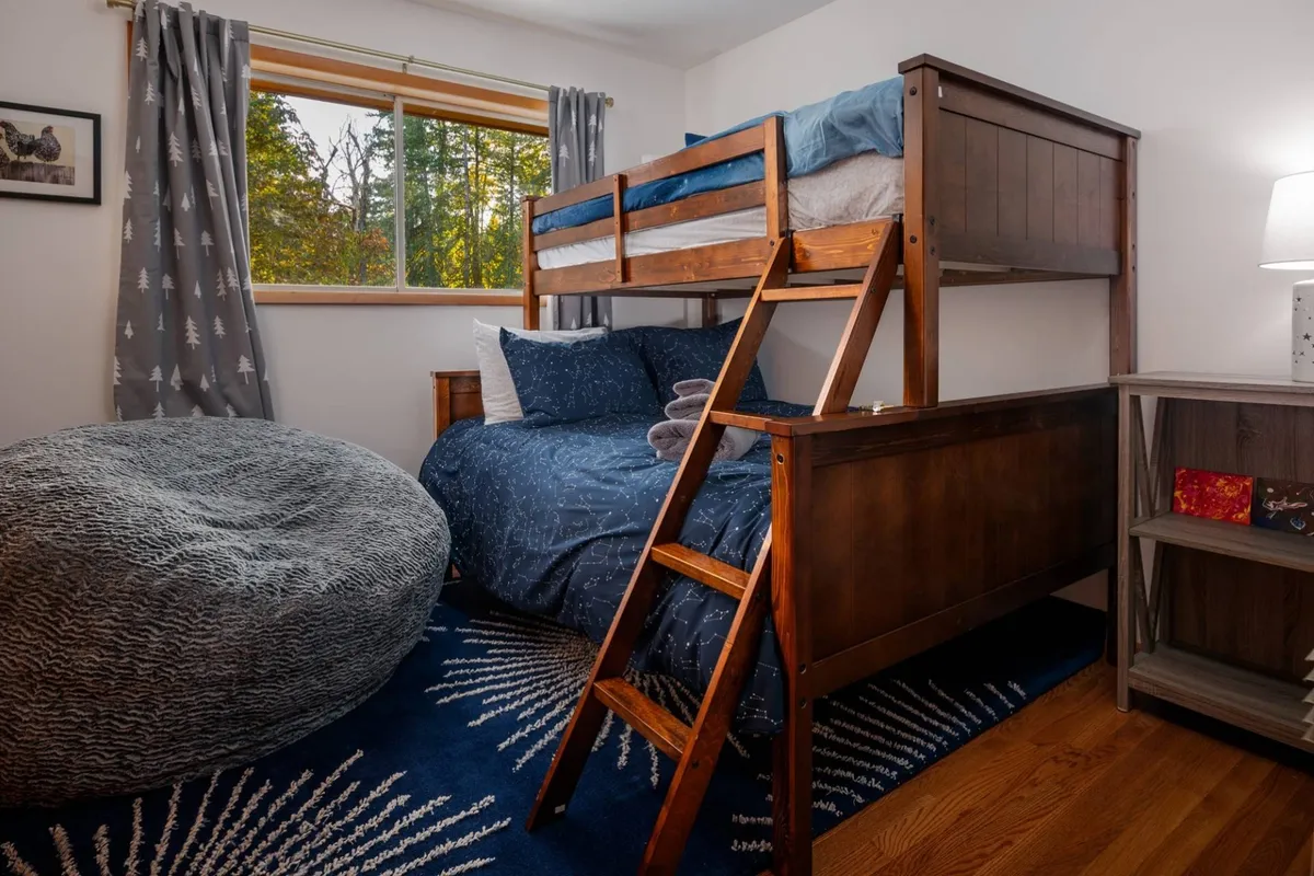 A playful bunk room with a twin-over-full bunk bed, a cheerful bean bag chair, a bright window, and a soft rug, creating a welcoming space ideal for kids and teens to play or rest.