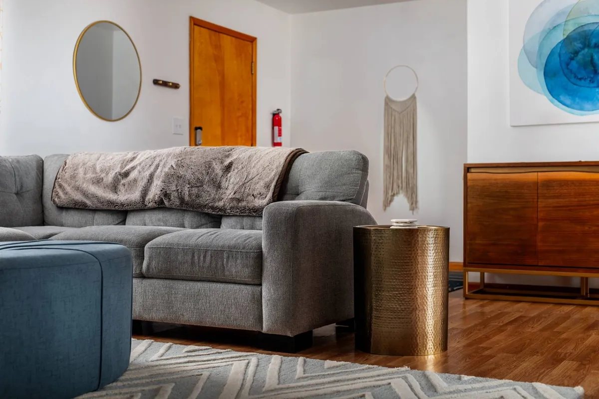 A welcoming living area with a gray couch, gold side table, textured wall hanging, and large mirror, styled with warm and modern touches. The space suggests relaxation after a day spent outdoors, with natural textures and colors echoing the surrounding landscape.